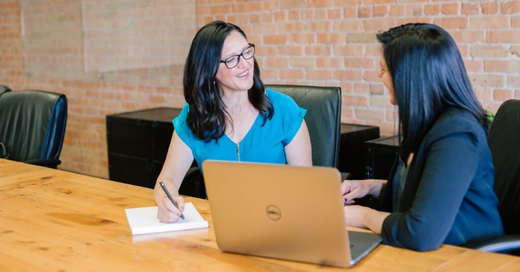 Two businesswomen consulting with each other in front of a computer.