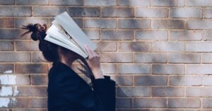 Woman in blue covering her face with a book.